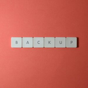 Close-up of keyboard keys spelling 'BACKUP' placed on a coral-colored surface.