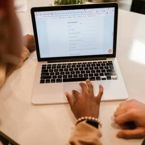 Two adults working together on a laptop displaying an online form, indoors.