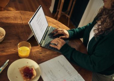 Photo by Microsoft Copilot Woman typing on laptop at wooden table with breakfast.